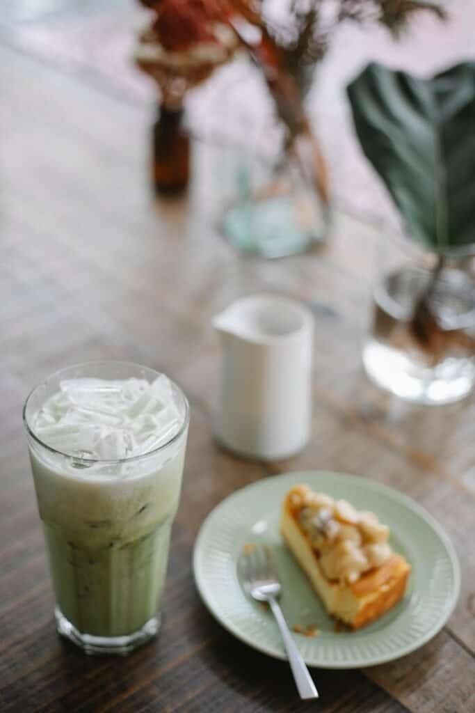 High angle refreshing iced matcha latte served on table with sweet cake slice in light room